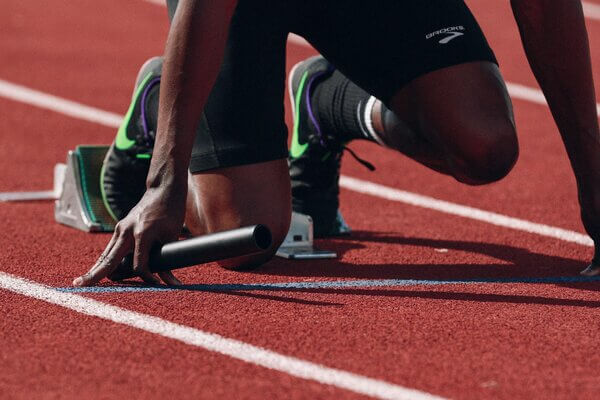 An athlete is poised for take-off in a track event, one knee on the ground, and the other above