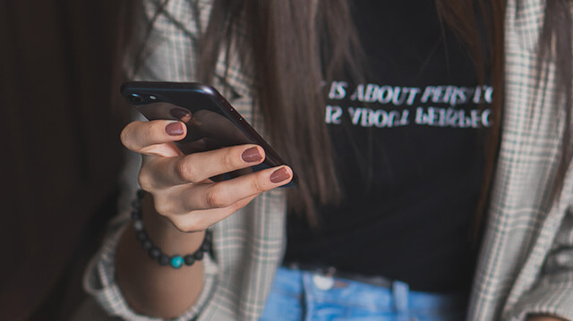 A young person is holding and using a cellphone in one hand