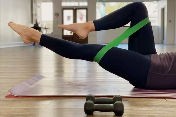 A woman is using an exercise band around her thighs as she performs leg raises