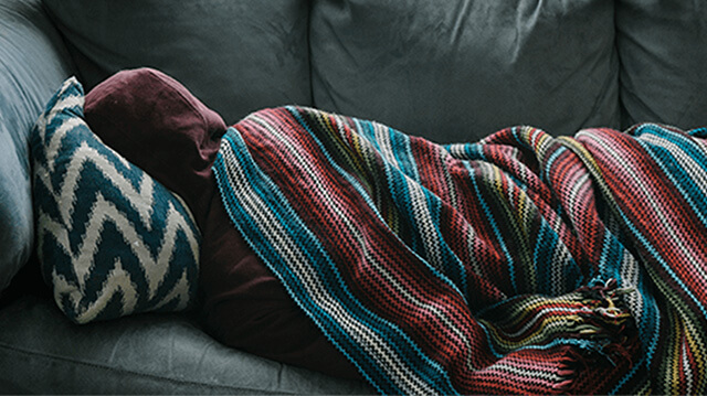 A person rests on a couch, wrapped up in a blanket